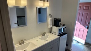 A bathroom with a double sink, a mirror, a towel rack, and a coffee maker. - Brownsville Motel (Brownsville)