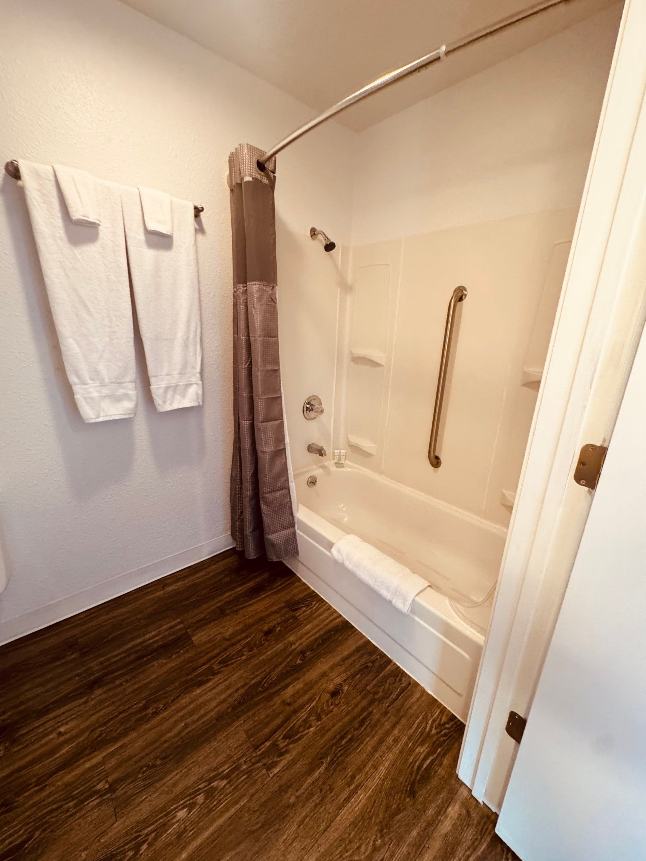 Baño con ducha, bañera y suelo de madera.
