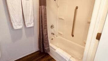 Baño con ducha, bañera y suelo de madera.