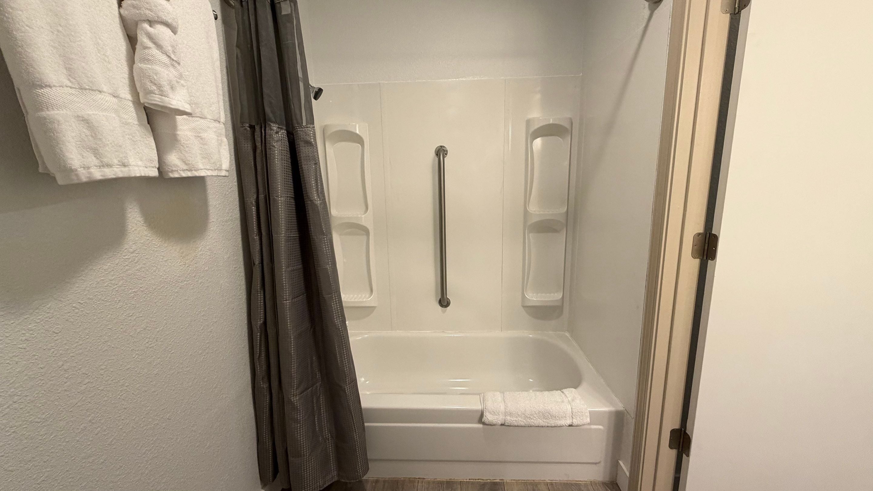 A bathroom with a bathtub, a shower with a grab bar, and a towel rack.