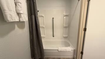 A bathroom with a bathtub, a shower with a grab bar, and a towel rack.