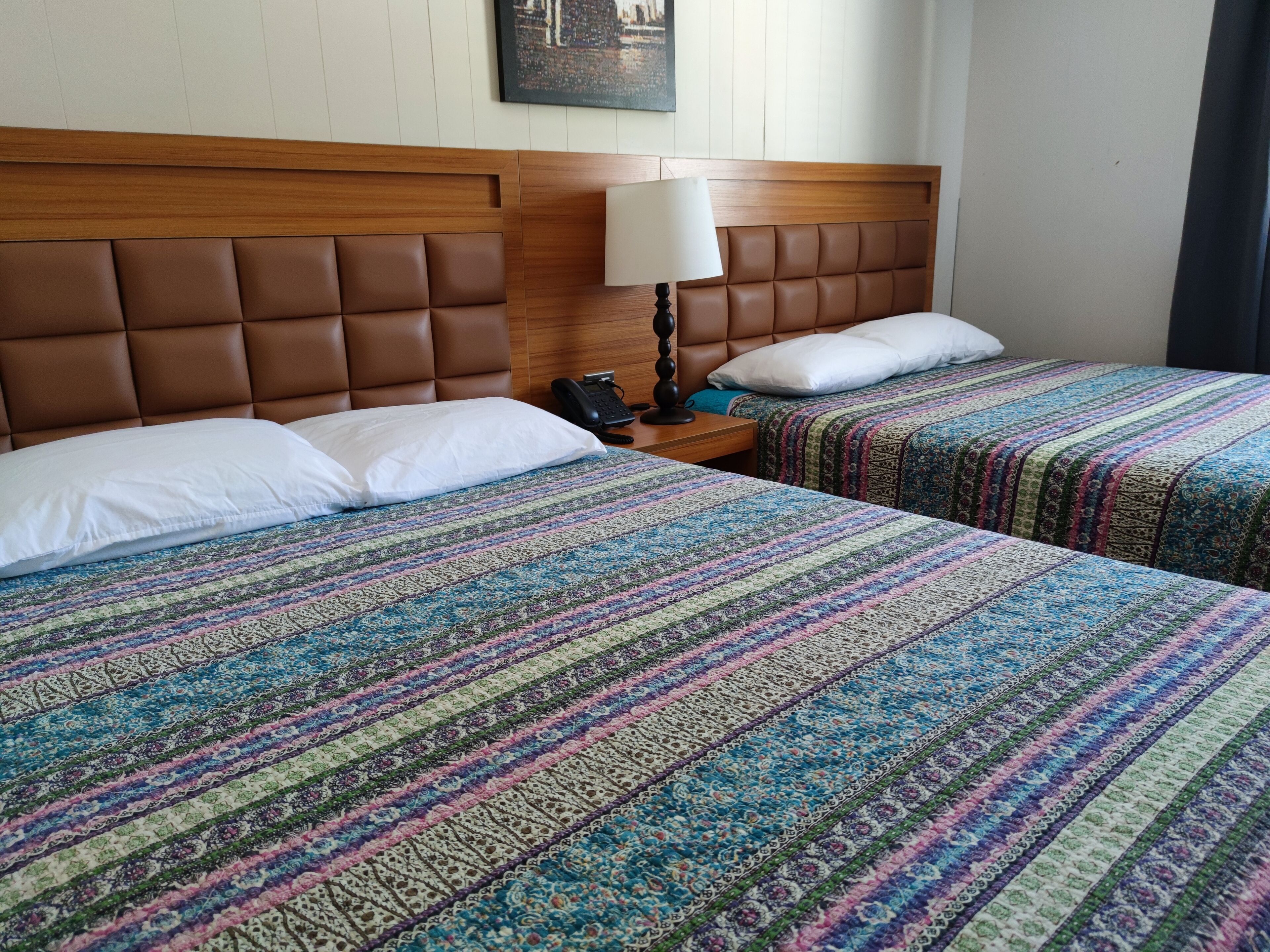 A hotel room with two beds, each with a striped bedspread, a wooden headboard, a bedside table with a lamp, and a telephone.