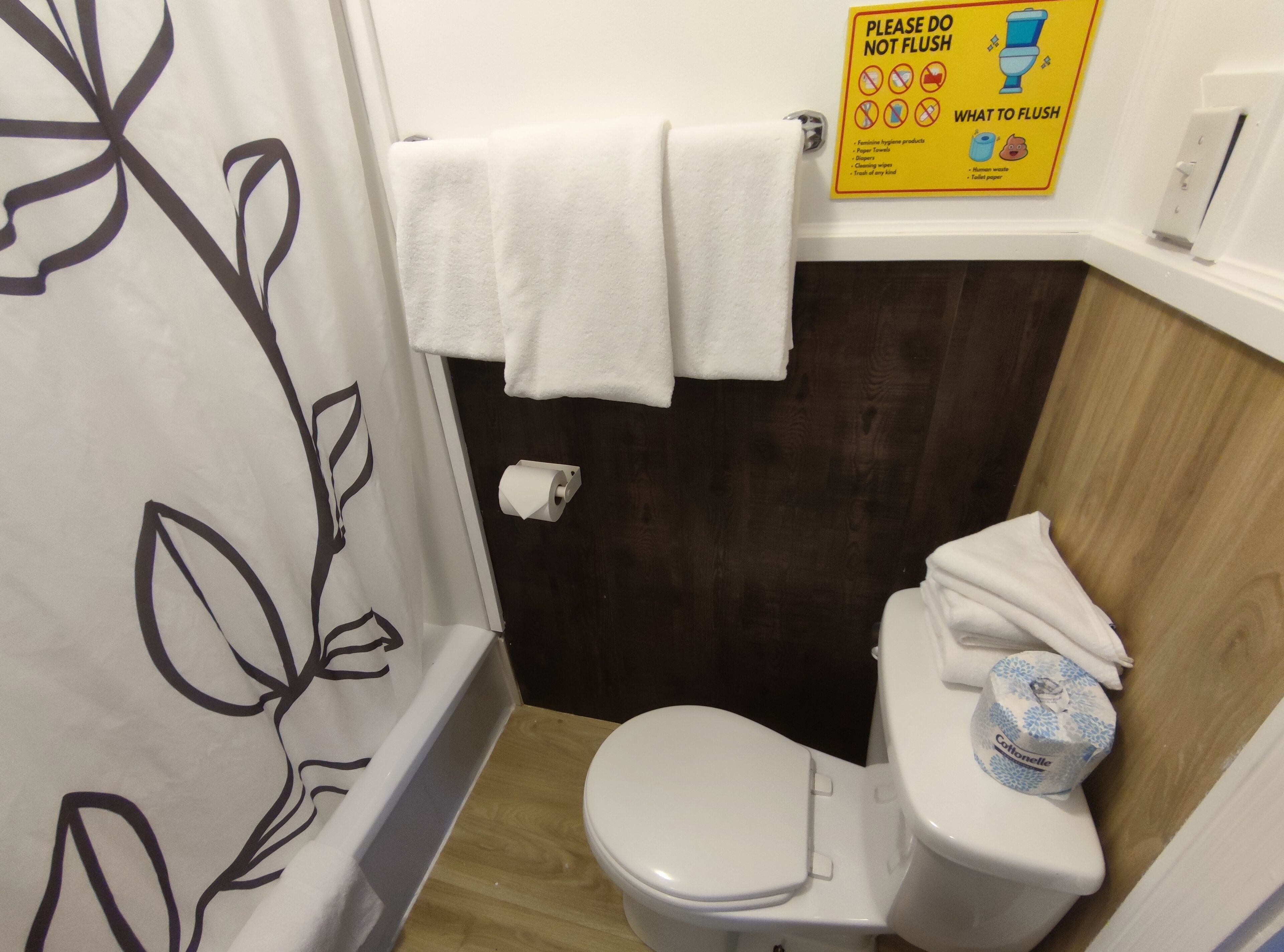 Une salle de bain avec des toilettes blanches, un rouleau de papier toilette et un panneau indiquant ce qu’il ne faut pas jeter dans les toilettes.
