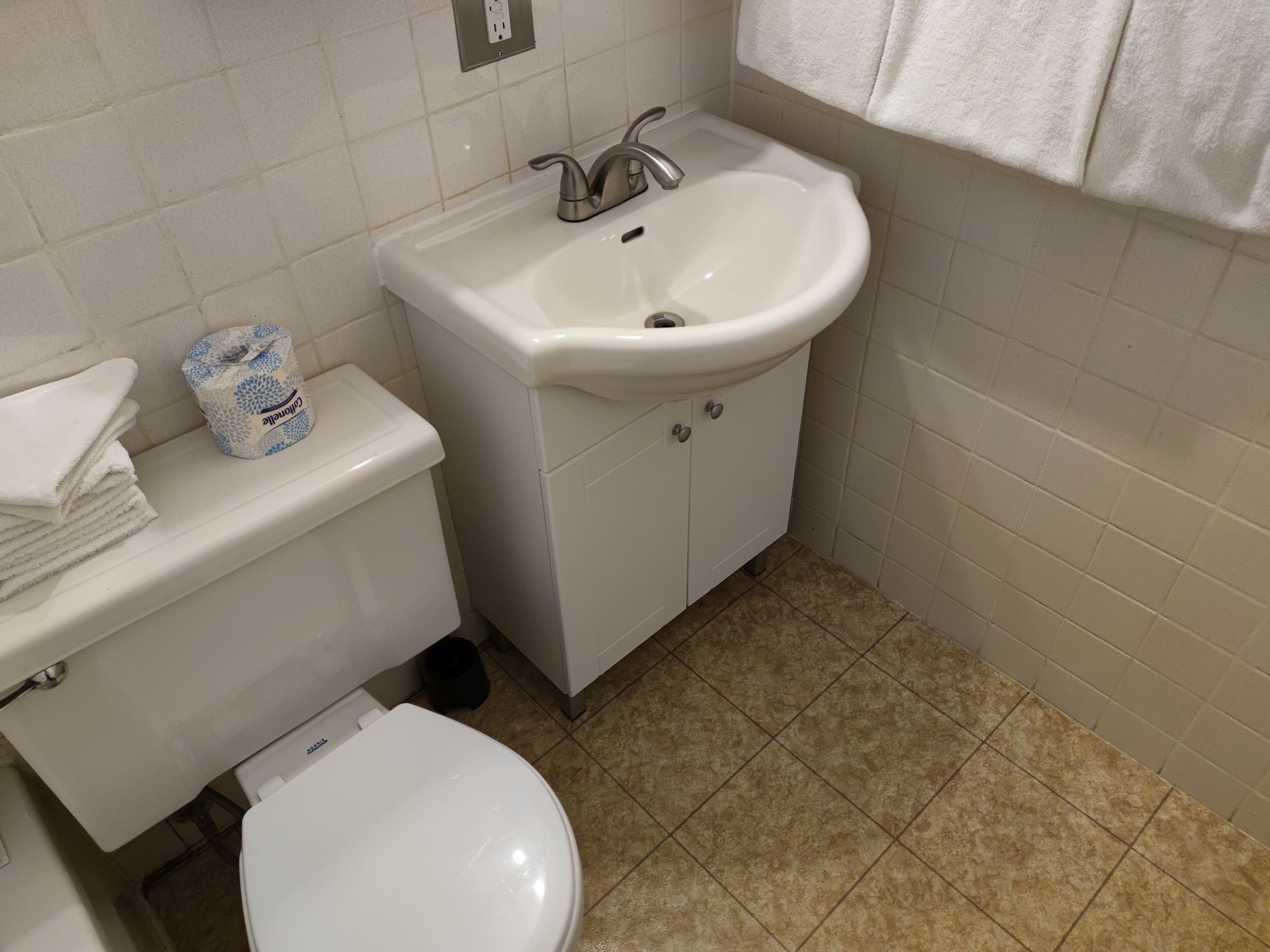 Un baño con un inodoro blanco, un lavamanos y una pila de toallas blancas.