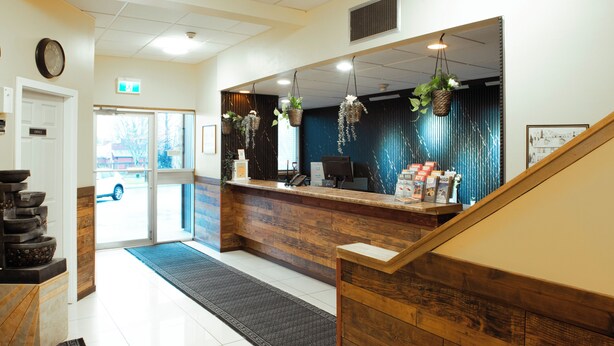 A reception area with a wooden reception desk, a clock on the wall, and a door leading outside. - Pemberton Hotel (Pemberton)