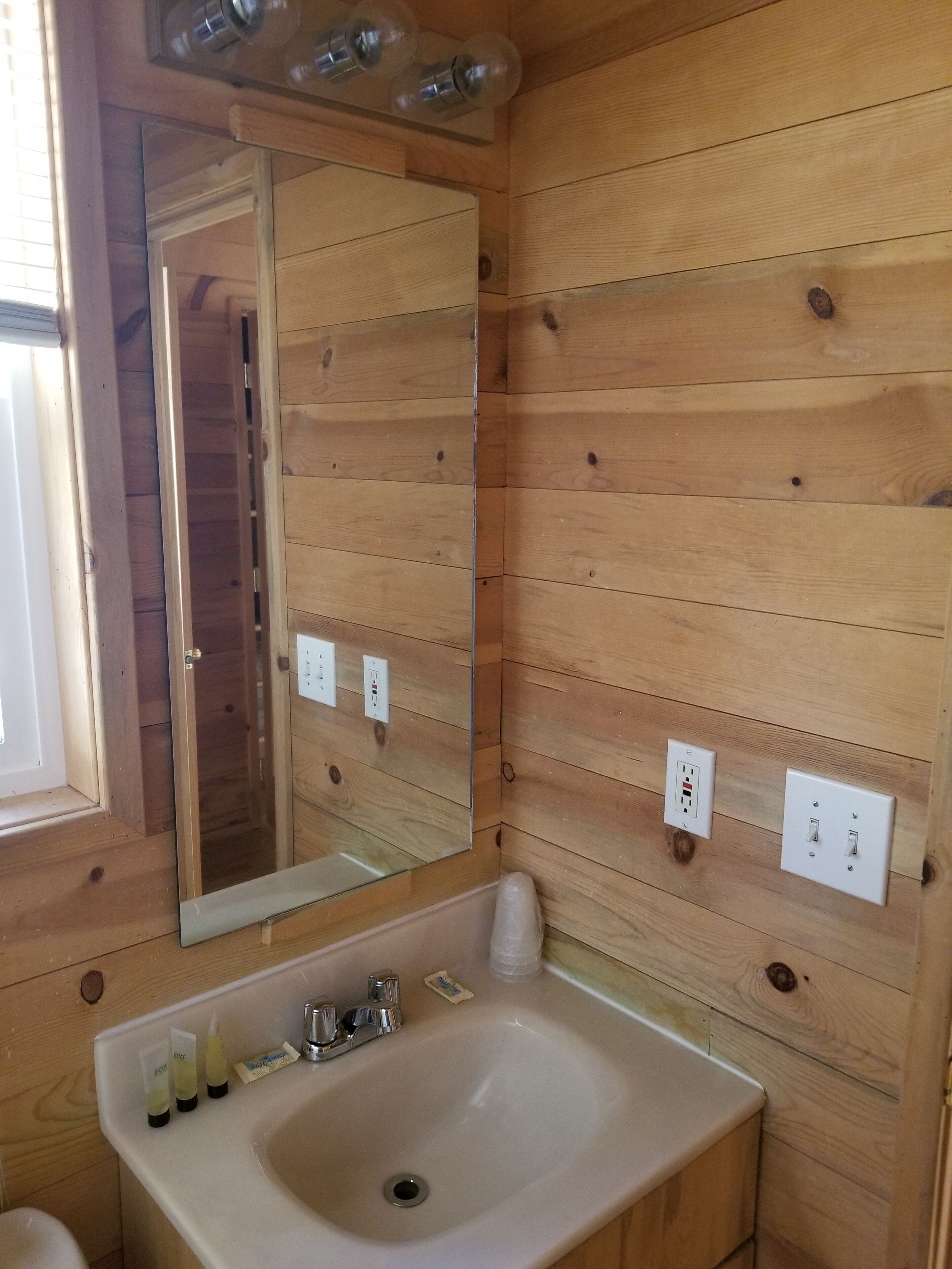 A wooden-paneled bathroom with a sink, mirror, and two electrical outlets.
