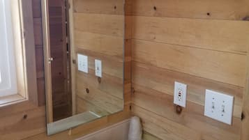 A wooden-paneled bathroom with a sink, mirror, and two electrical outlets.