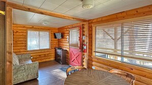 A wooden cabin interior with a dining table, chairs, a sofa, and a fireplace. - Sourdough Lodge (Lowman)