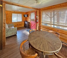 Interior de una cabaña de madera con una mesa de comedor, sillas, un sofá y una chimenea.