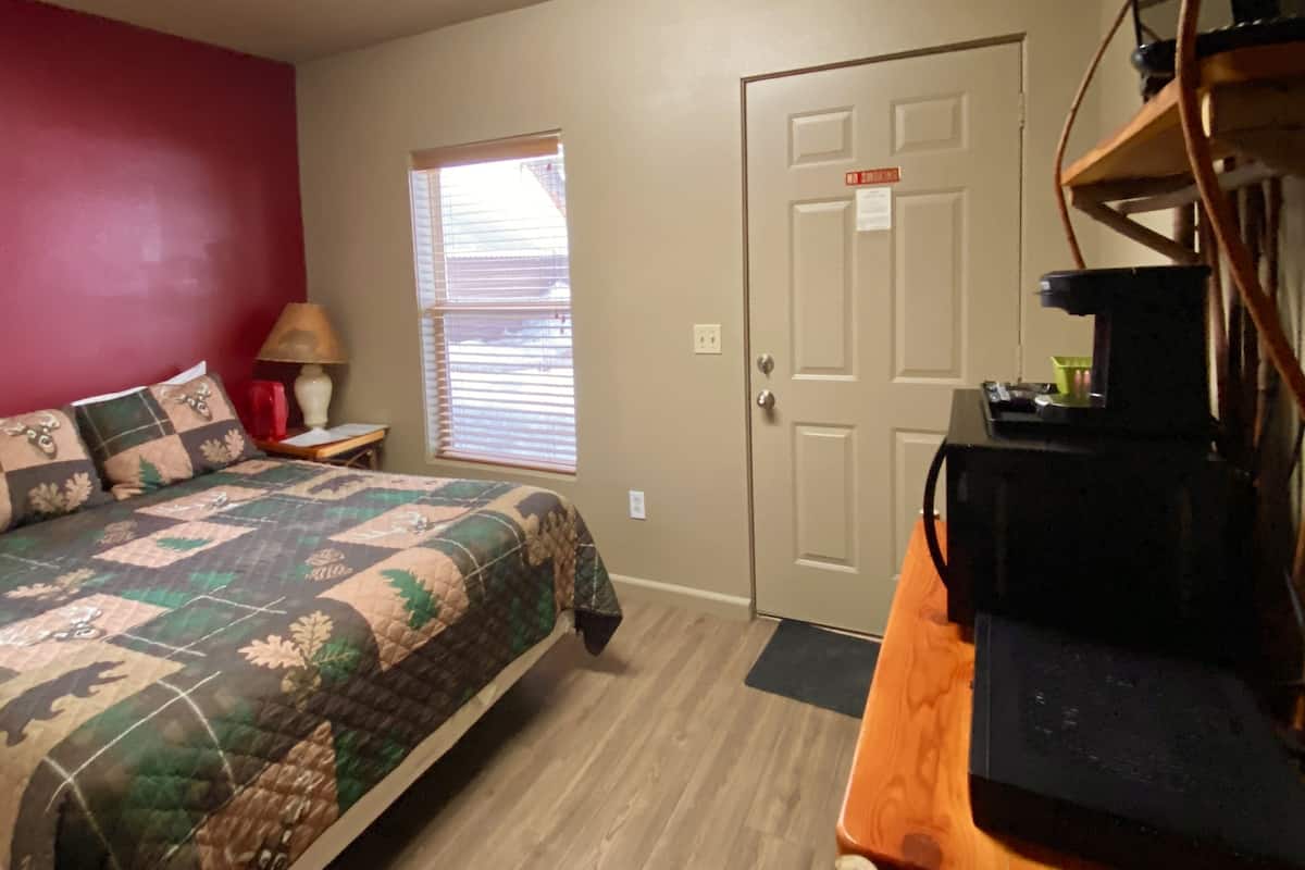 A bedroom with a bed, a desk, a lamp, a door, and a window.