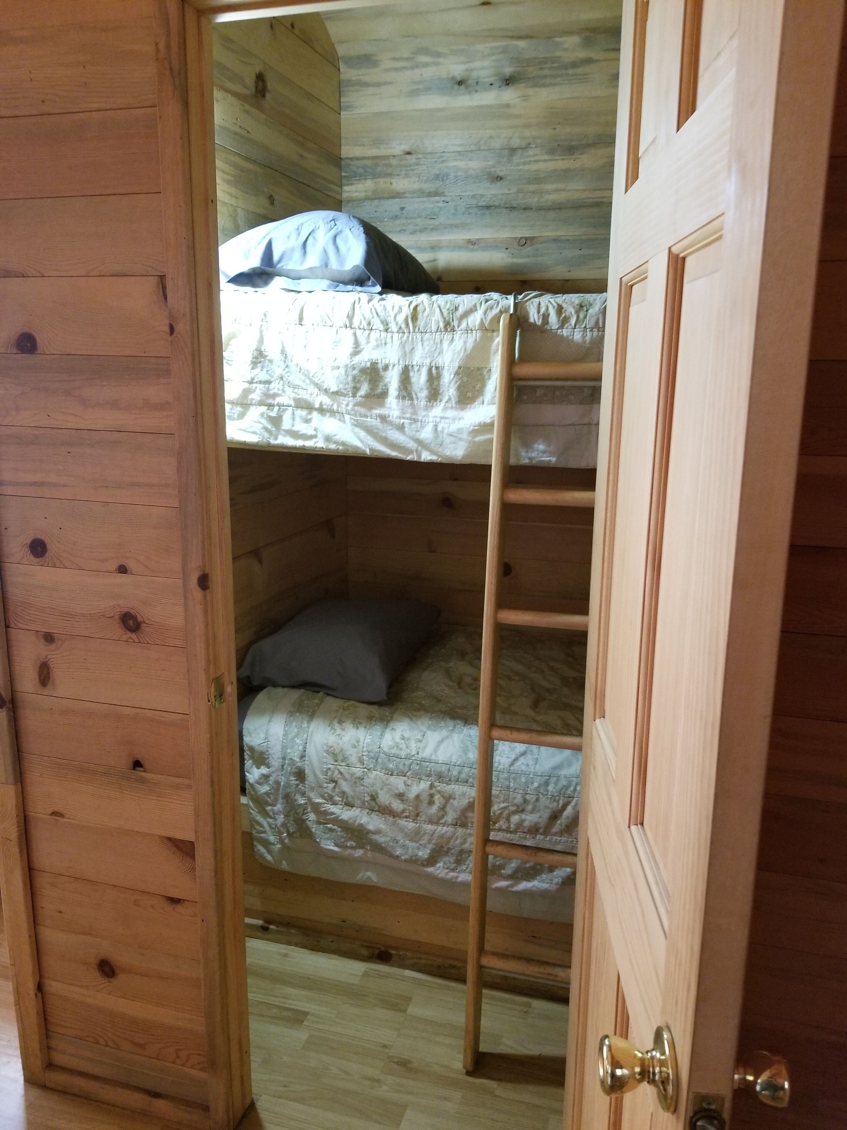 A wooden bunk bed room with a ladder, a pillow, and a door.