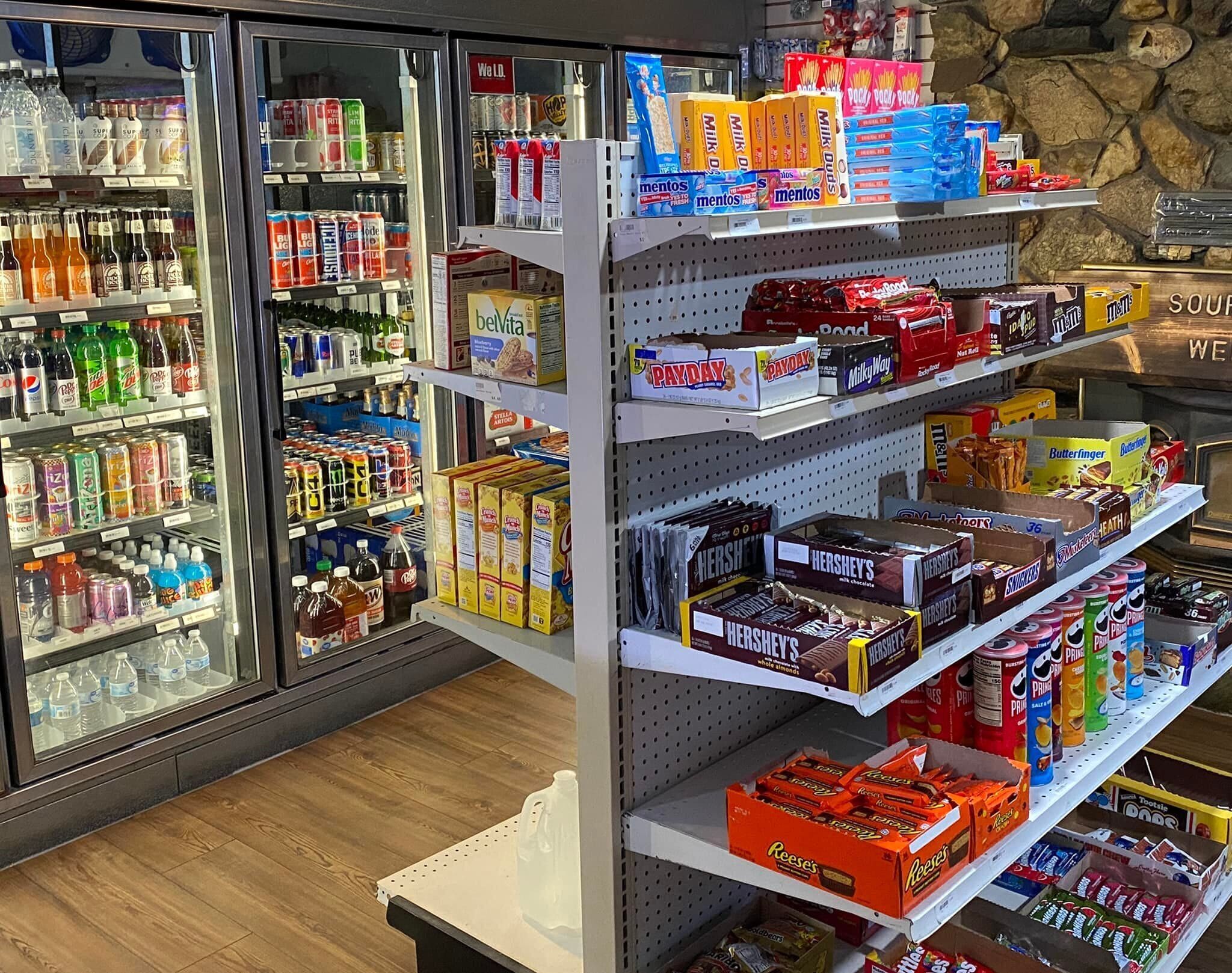 Una tienda de comestibles con bebidas frías, aperitivos y productos envasados en estantes.