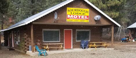 A log cabin with a sign for Sourdough Lodge Motel, featuring a red door, two windows, and a satellite dish.