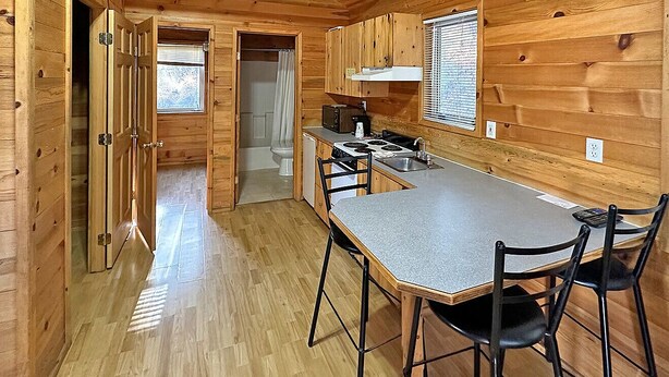 A compact kitchen with wooden walls and a central island, a sink, and a stove. - Sourdough Lodge (Lowman)