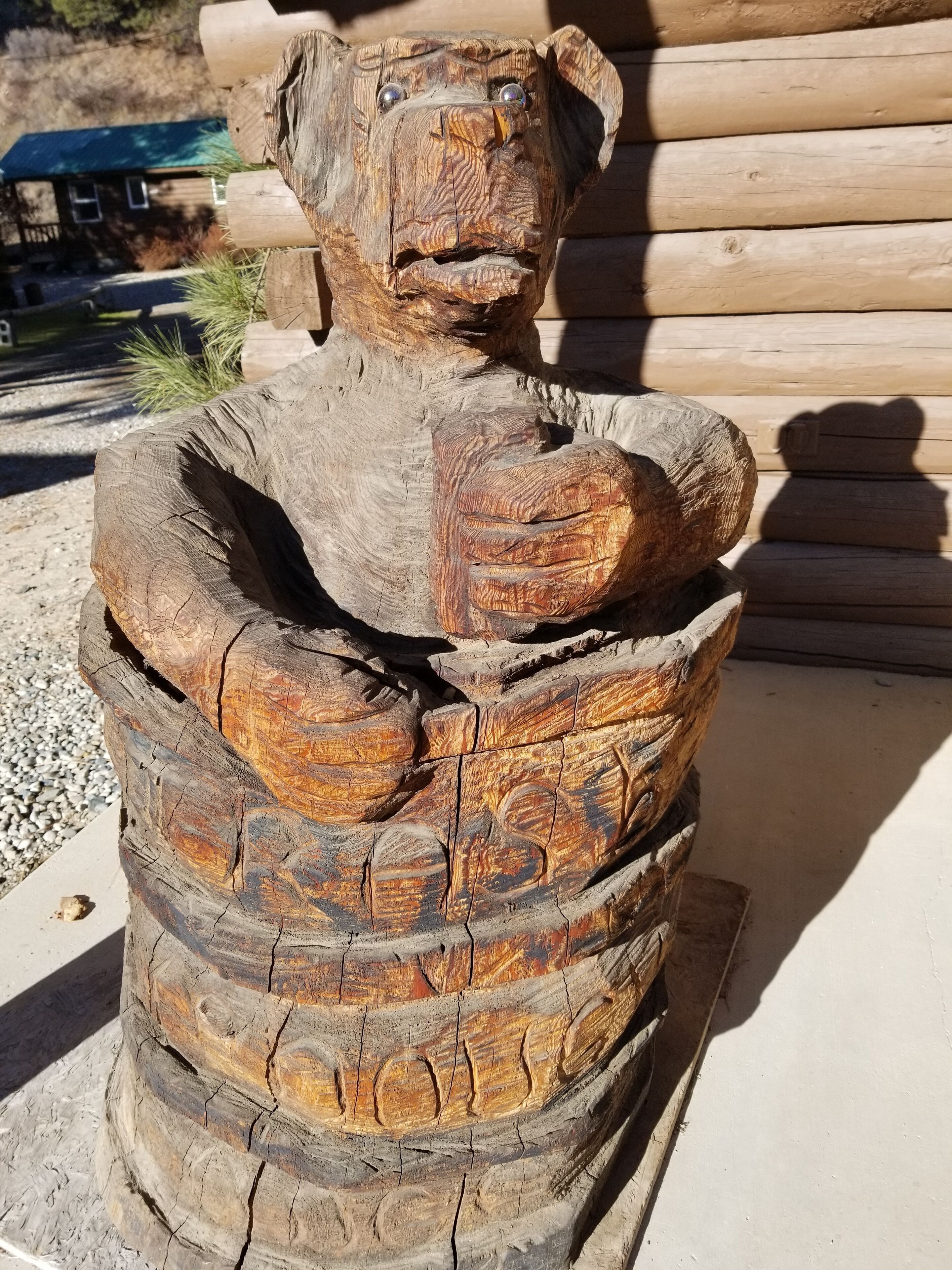 Eine hölzerne Bärenskulptur mit leerem Inneren, draußen vor einem Holzschienbestand.