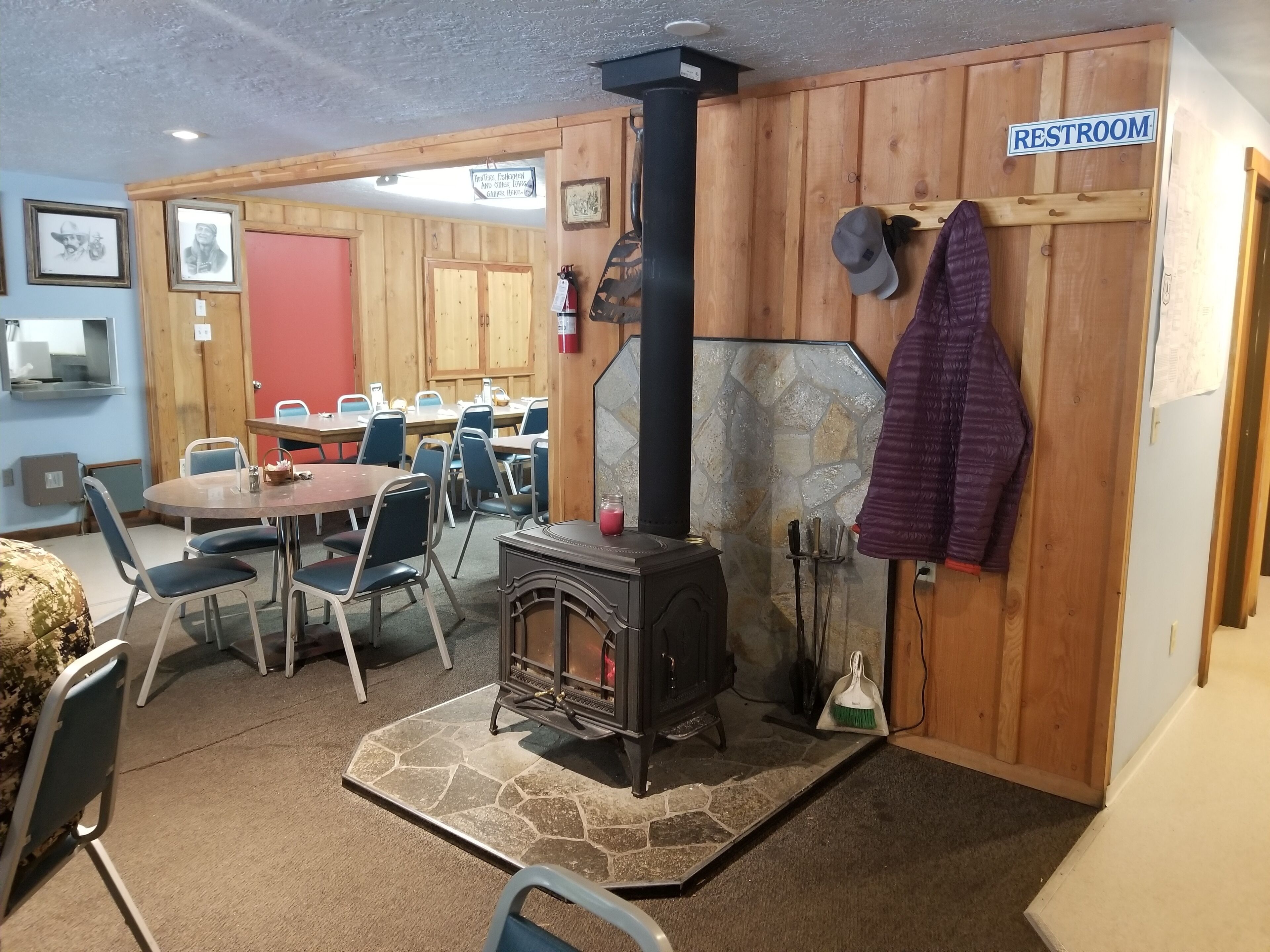 Une pièce chaleureuse avec une cheminée en pierre, une table avec des chaises, un panneau indiquant les toilettes et une porte en bois.