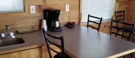 A wooden interior with a kitchen area, including a sink, a coffee maker, and a dining table with chairs.