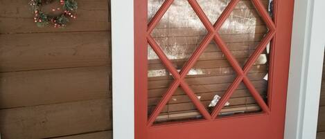 A red door with a diamond pattern window, a 'C' sign above it, and a wreath on the wall to the left.
