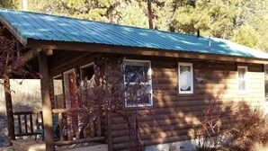 A rustic cabin with a covered porch, wooden logs, and a gravel driveway. - Sourdough Lodge (Lowman)