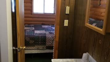 A wooden cabin interior with a bathroom featuring a sink, mirror, and a window with a view of a forest.