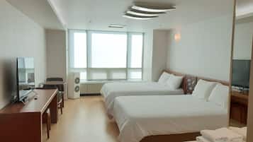 A hotel room with two beds, a desk with a chair, a television, and a large window providing natural light.