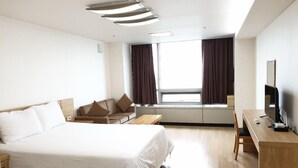 A hotel room with a large bed, a desk with a TV, and a window with curtains. - Goodday Airtel (Incheon)