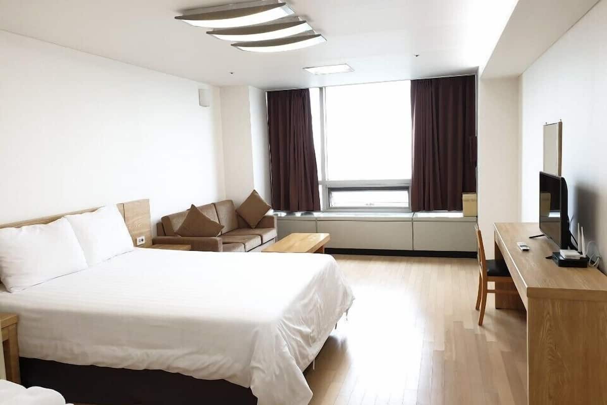 Habitación de hotel con una cama grande, un escritorio con televisor y una ventana con cortinas.