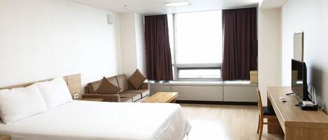 A hotel room with a large bed, a desk with a TV, and a window with curtains.