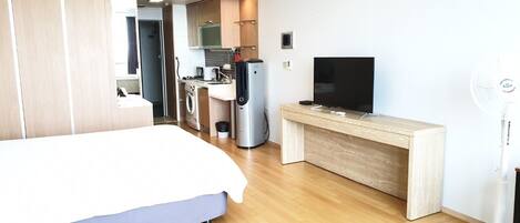 Une chambre d’hôtel moderne équipée d’un lit, d’un bureau avec télévision, d’une kitchenette et d’un ventilateur.
