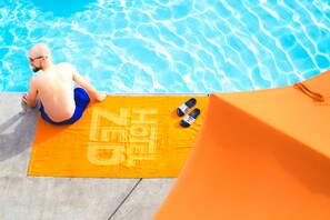 A man sitting on a towel by a pool with a bottle and a cap on it. - Hotel Zed Kelowna (Kelowna)