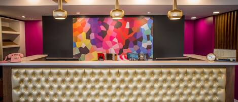 A reception area with a tufted gold headboard, a colorful geometric wall art, and three pendant lights.