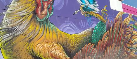 Une fresque colorée représentant un coq, peinte sur le mur d’un immeuble.