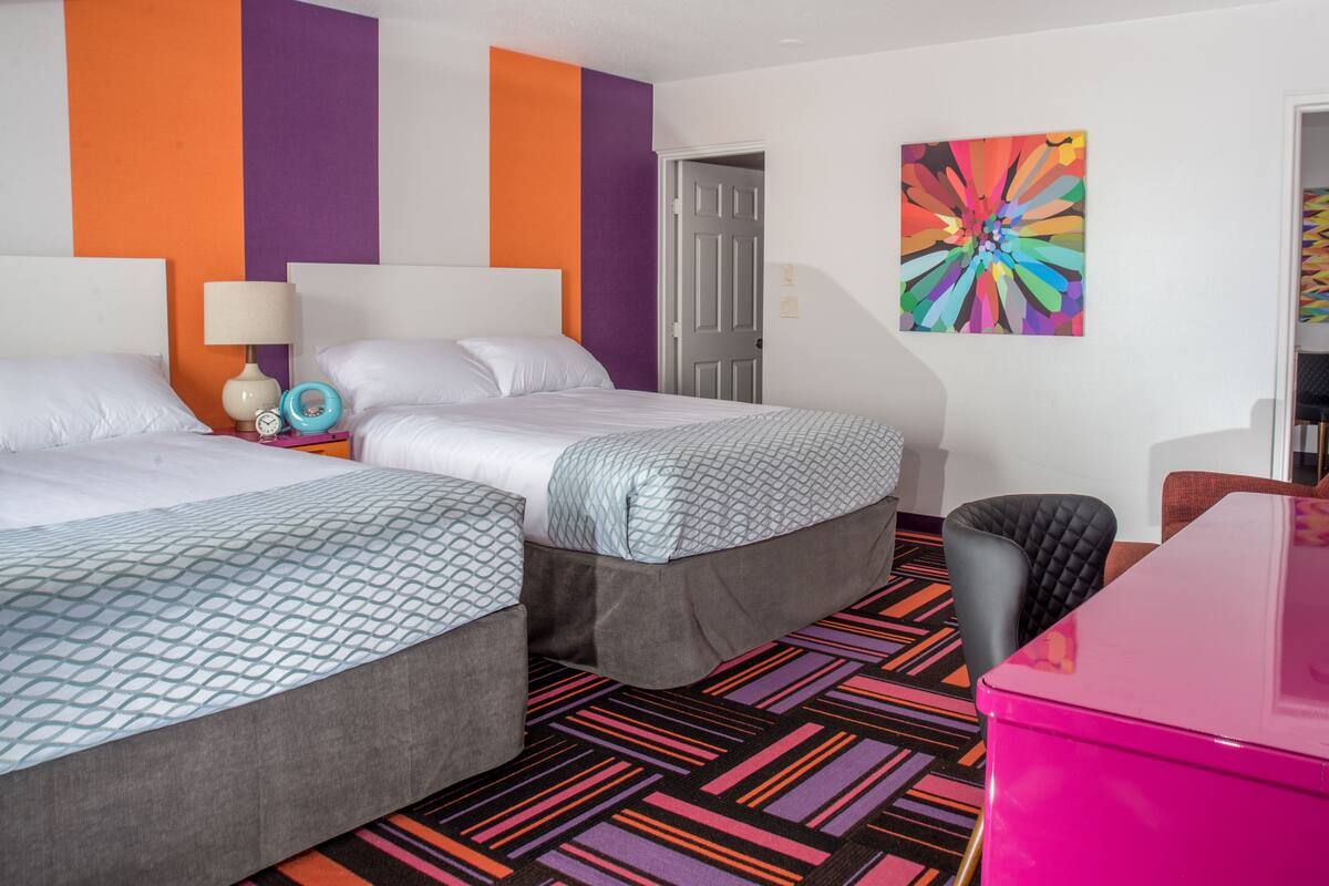 A hotel room with two beds, a colorful abstract painting, and a vibrant patterned carpet.