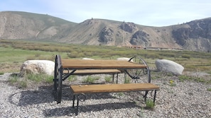 A rustic outdoor seating area with a wooden table and bench, surrounded by rocks and gravel, set against a backdrop of mountains and sparse vegetation. - Valley Creek Lodge (Stanley)