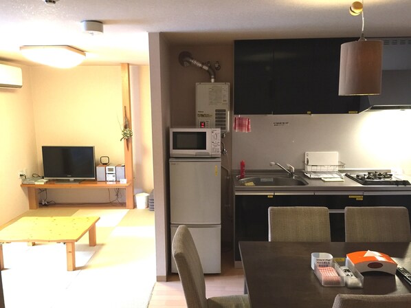 A compact kitchen with a microwave, stove, and sink. There's a dining table with chairs and a small bench.