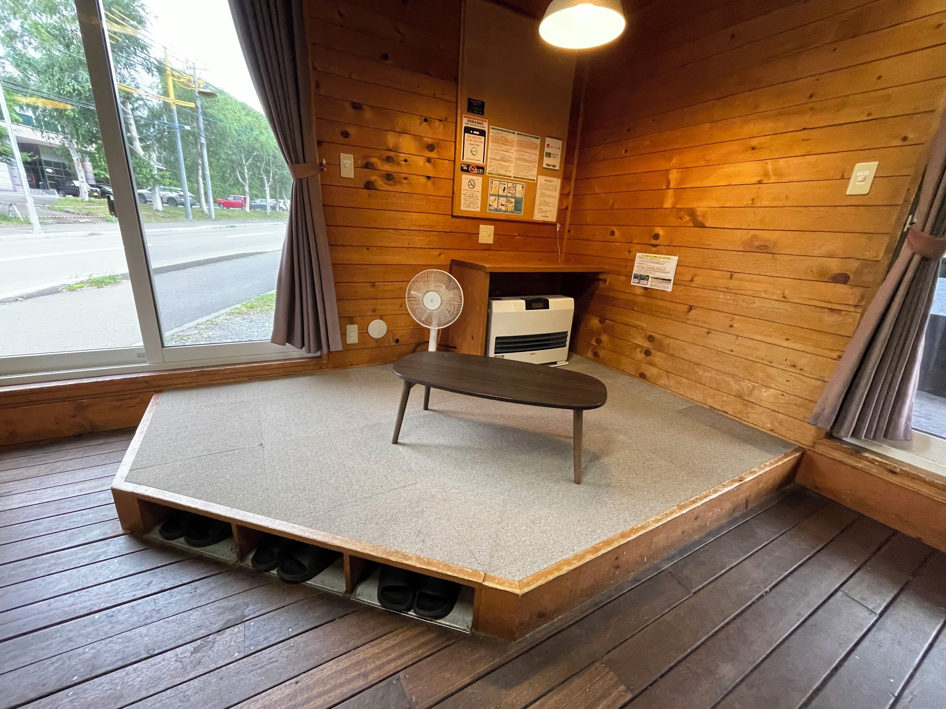 Un interior de madera con un banco, un ventilador y una ventana con cortinas.