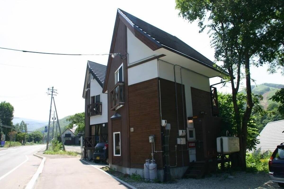 A two-story building with a sloped roof, a visible garage, and a small outdoor area with a car parked nearby.