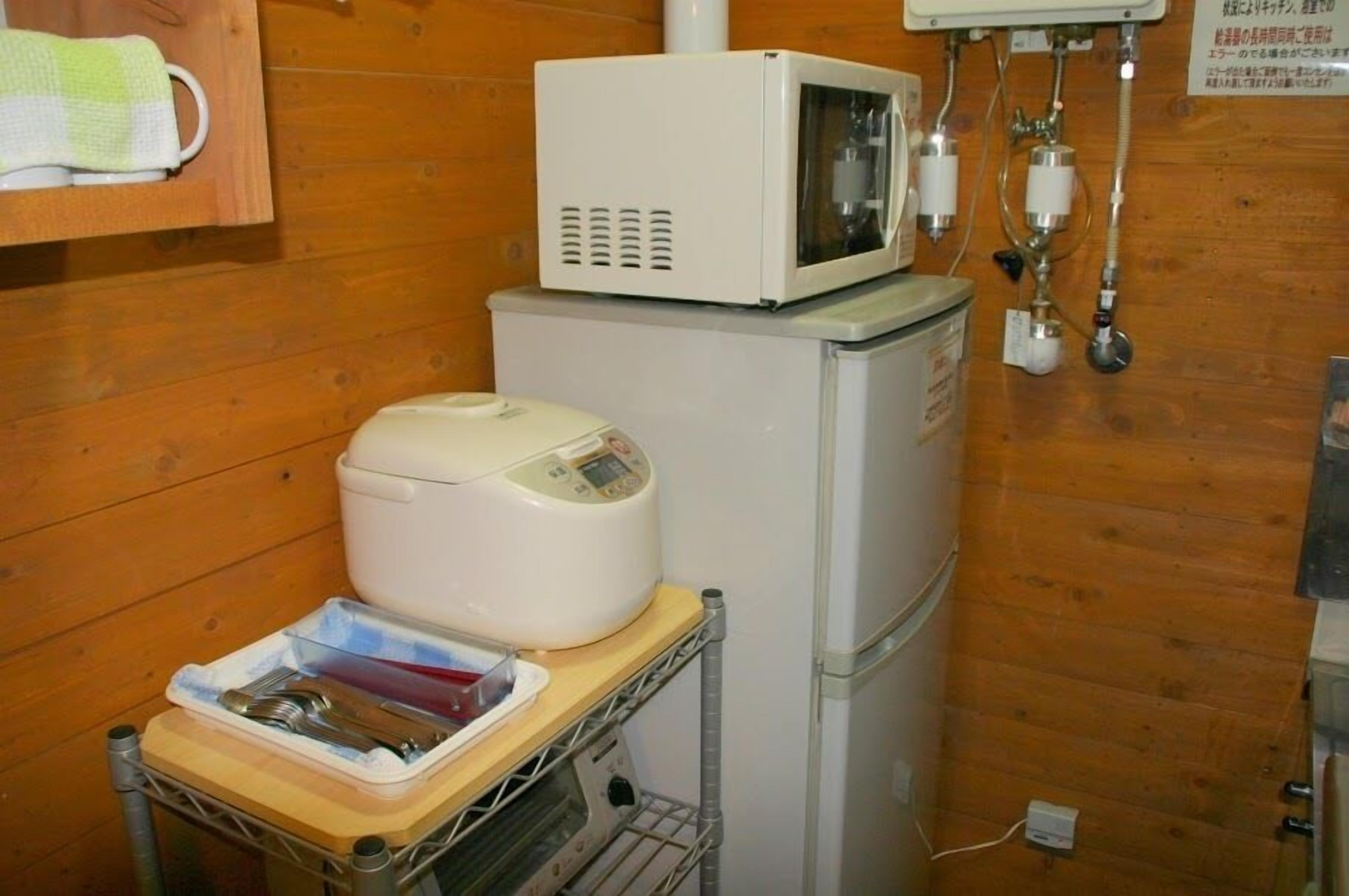 A compact kitchen with a microwave, a small refrigerator, and a food warmer on a wooden countertop.