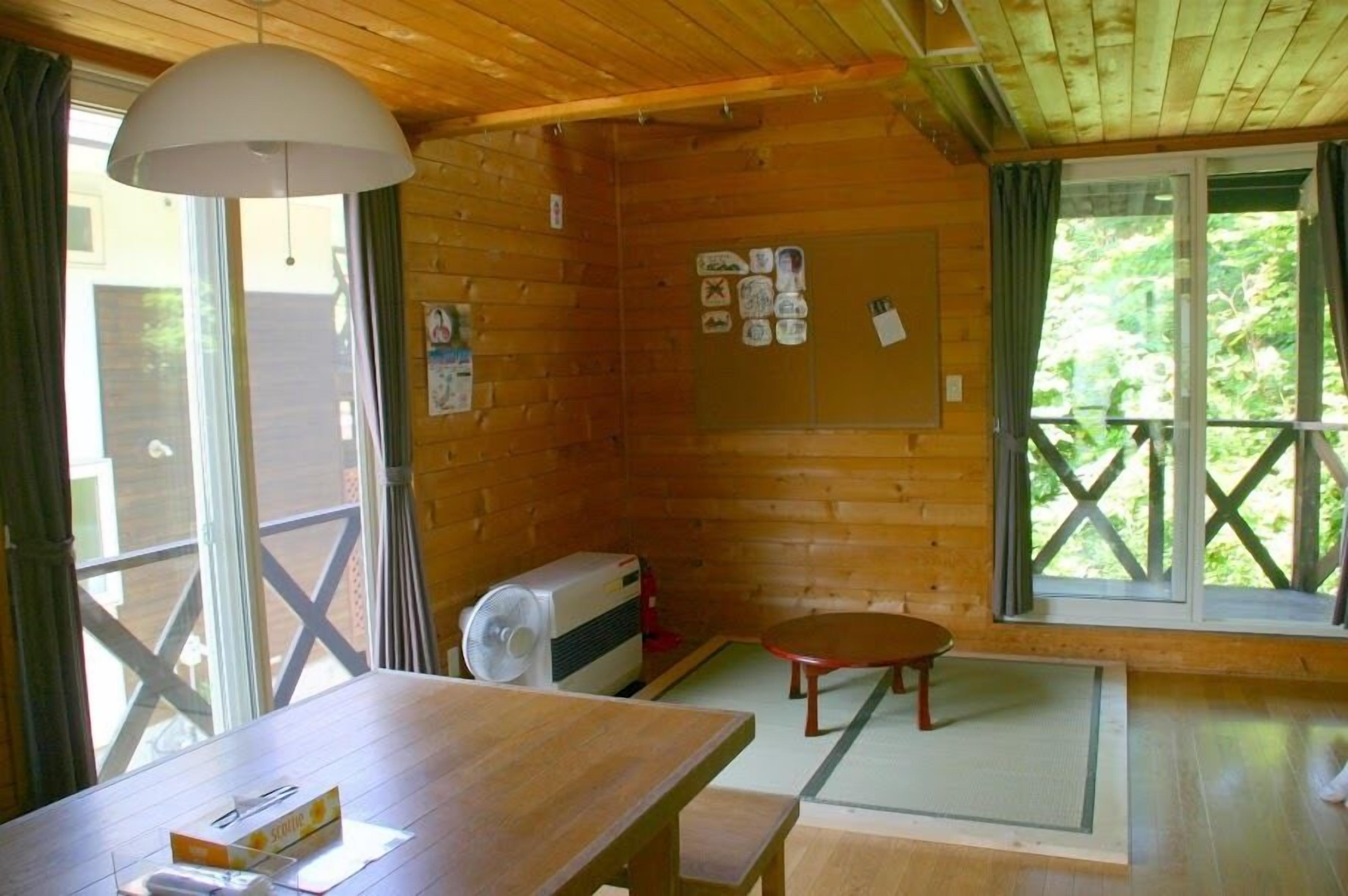 A wooden cabin with a dining table, a fan, and a bulletin board with various notices.