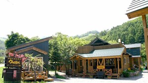 A rustic wooden building with a porch, surrounded by greenery and hills. - Winkel Village (Otaru)