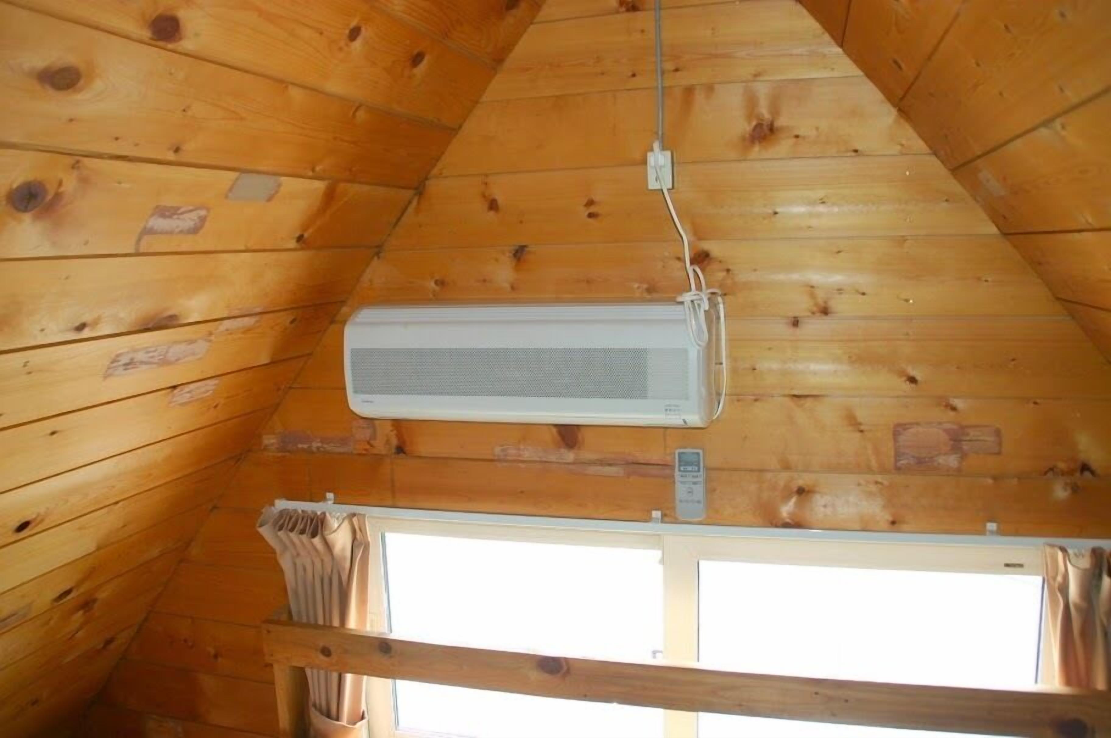 A wooden cabin interior with a sloped ceiling, a mounted air conditioning unit, and a window with curtains.