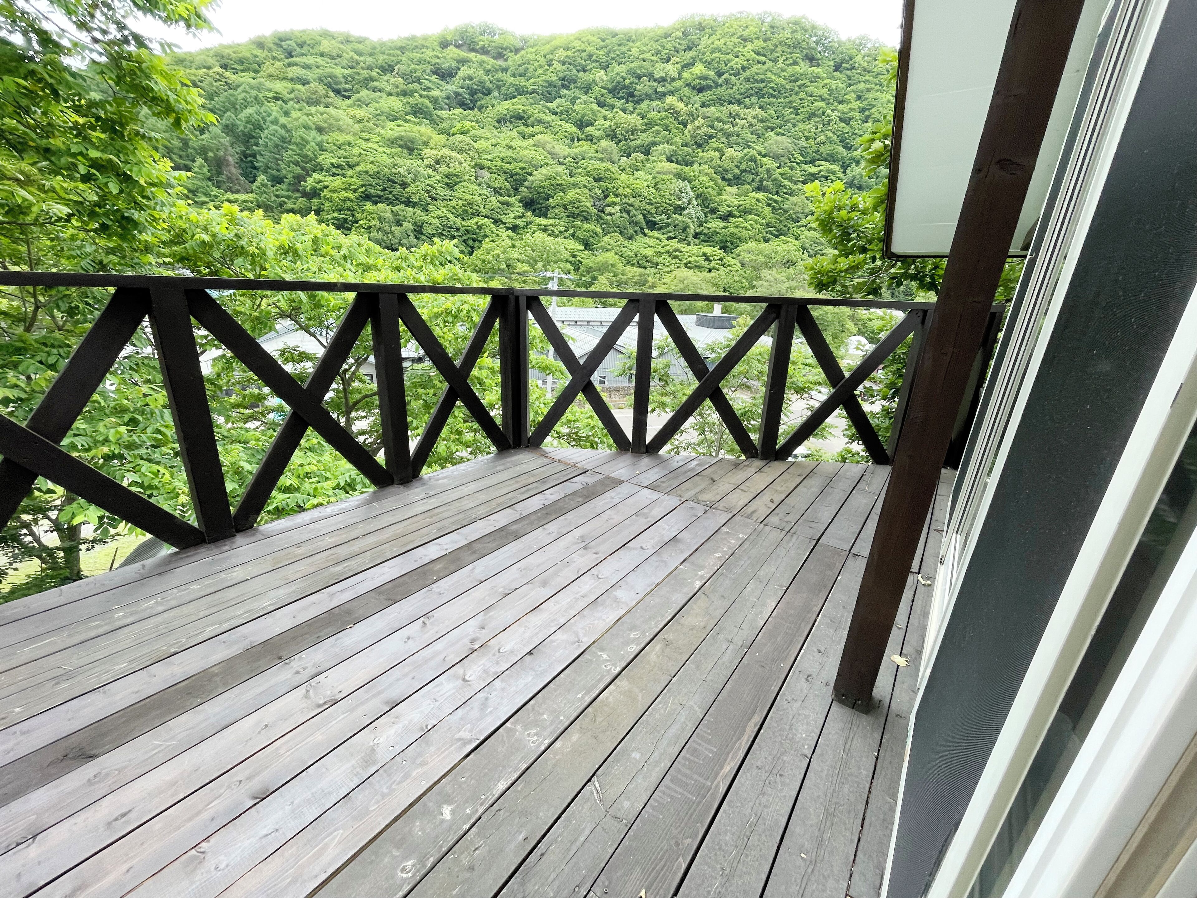 Eine Holzterrasse mit schwarzer Brüstung, die auf einen bewaldeten Bereich blickt.