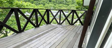 Eine Holzterrasse mit schwarzer Brüstung, die auf einen bewaldeten Bereich blickt.