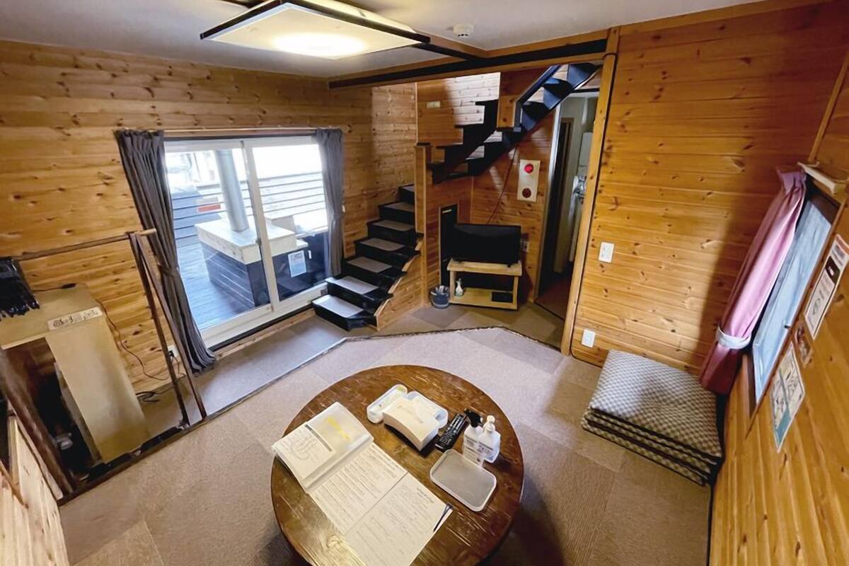 A wooden cabin interior with a dining table, a staircase, and a large window.