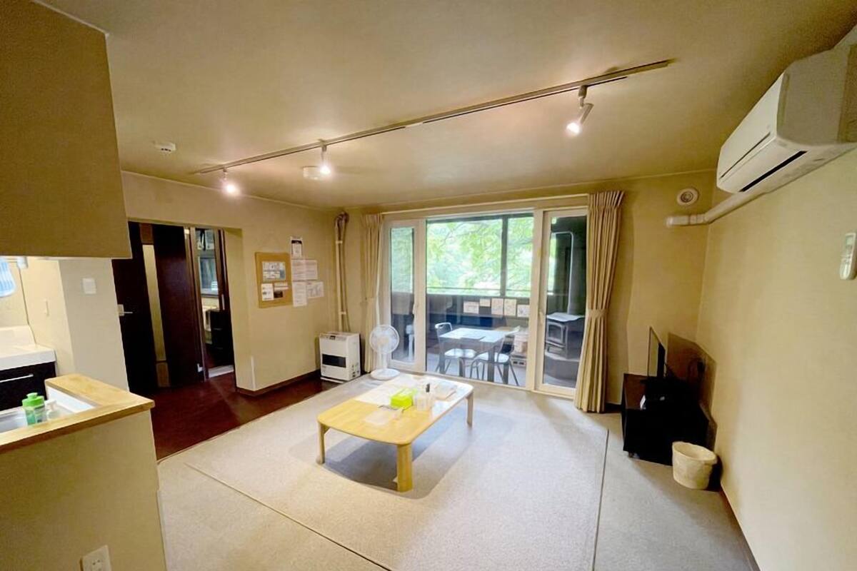 A spacious room with a large sliding glass door leading to an outdoor area, a small table, and a kitchenette area.