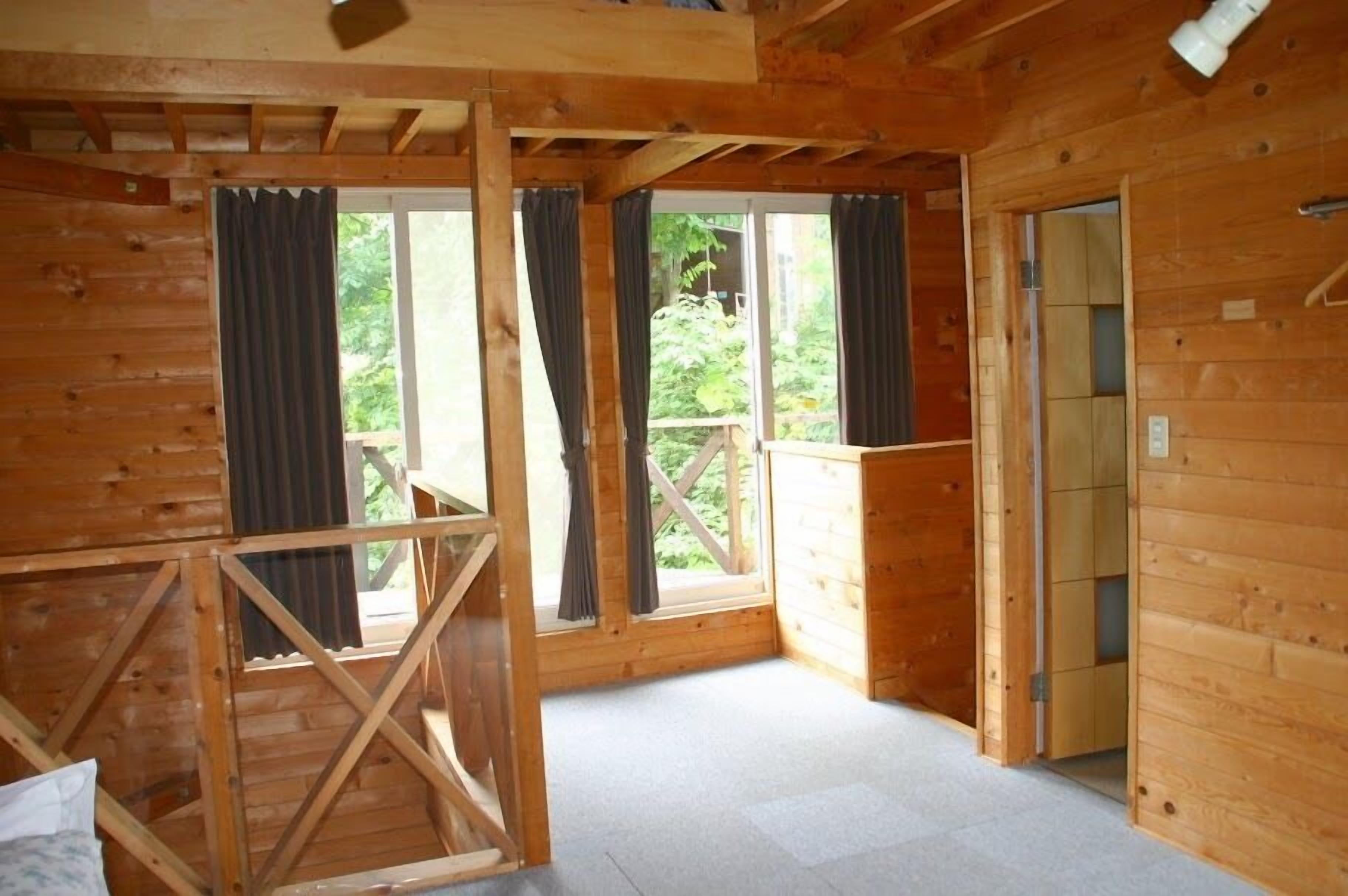 A wooden cabin interior with large windows, a wooden staircase, and a door leading outside.
