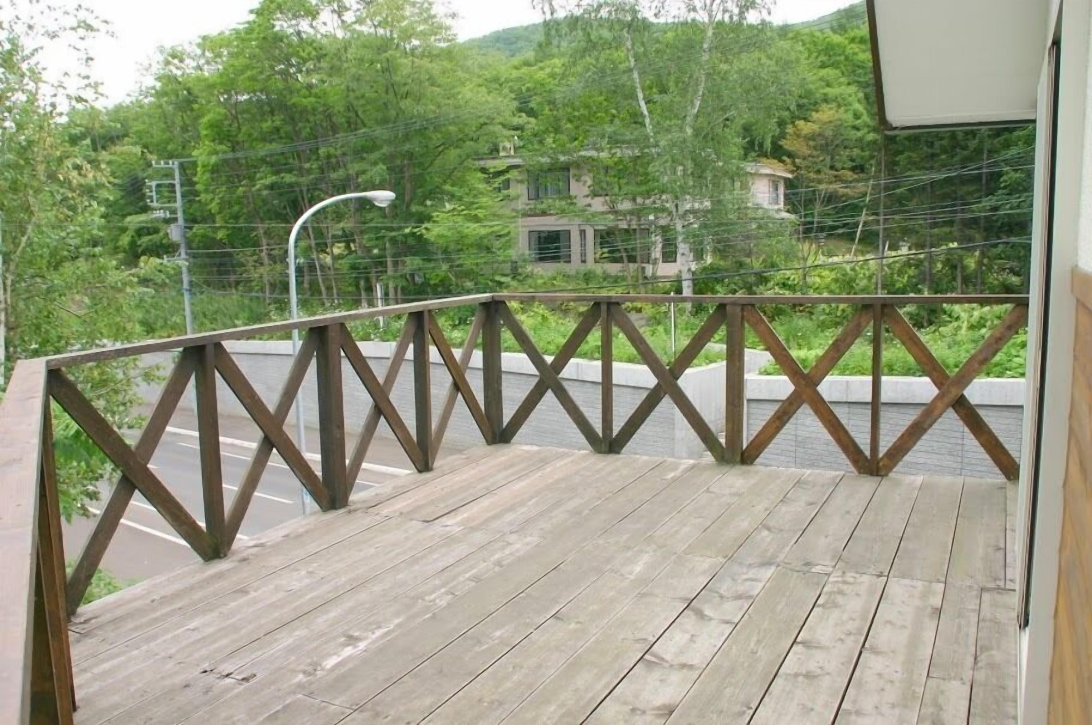 Eine Holzterrasse mit Metallgeländer, mit Blick auf eine Straße und Grünflächen.