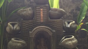 Een stenen constructie met een centrale nis waarin een zittende figuur staat, aan weerszijden van twee grote vazen en twee kleinere vazen op voetstukken.