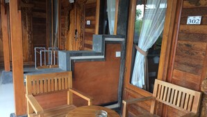 Een houten chalet met een bord met nummer 302, een houten bankje, een klein rond tafeltje en een raam met gordijnen.