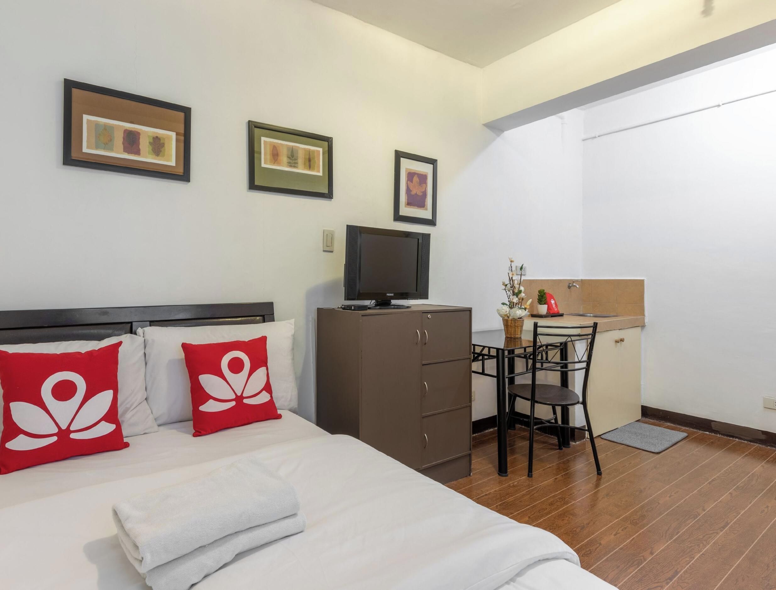 A hotel room with a bed, a desk, a television, and a small kitchenette.